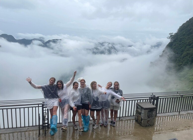 Un groupe de personnes se tient sur un quai mouillé, protégé par une rambarde, et surplombe une vallée enveloppée de nuages. 3