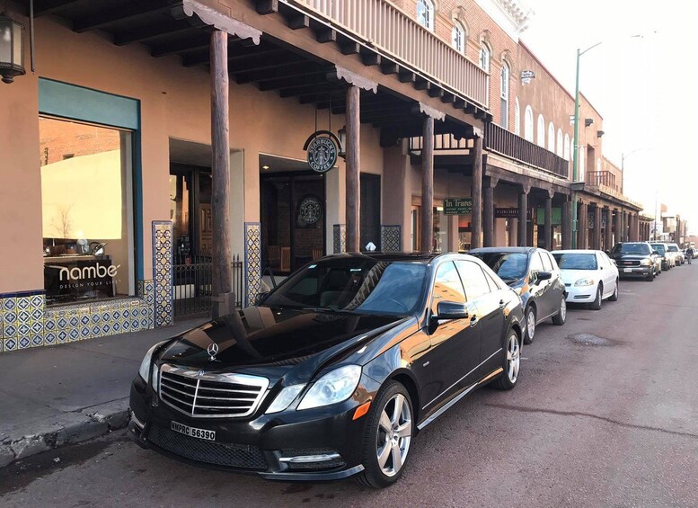 Un Mercedes-Benz negro estacionado en una calle con locales comerciales, incluyendo una Starbucks y una tienda Nambe. 1