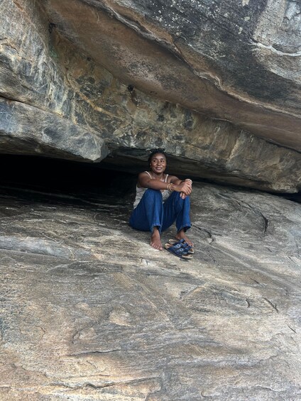 A person sitting on a rocky surface with a cave entrance in the background. 2