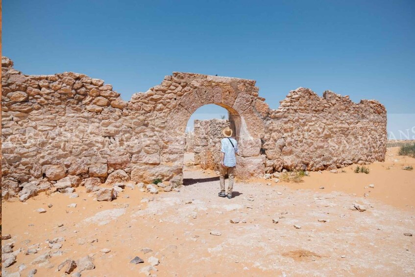A person standing in front of ancient stone ruins with a large archway. 1