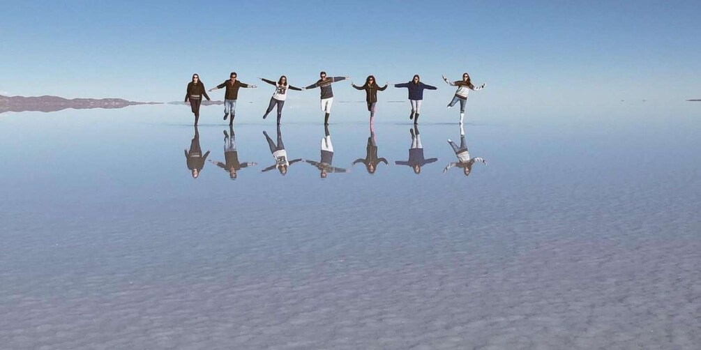 Un groupe de personnes se tient sur une étendue de sel plane et réfléchissante, les bras tendus, créant ainsi une image symétrique. 1
