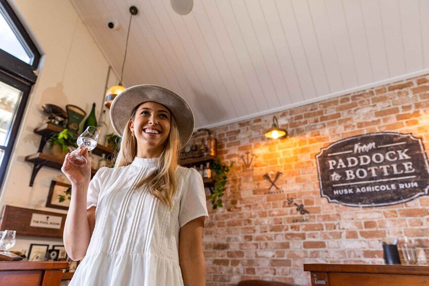 Una persona tiene un bicchiere di vino in un ambiente rustico con un muro in mattoni e un cartello che recita 'from Paddock Bottle HUSK AGRICOLE RUM'. 4