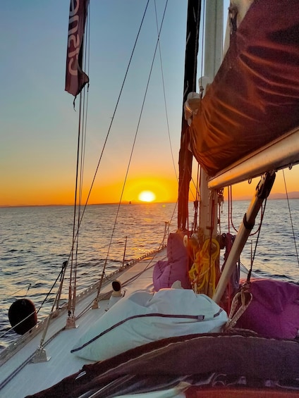 Ein Segelboot bei Sonnenuntergang, die Sonne ist nahe am Horizont, mit Seilen und einer Flagge. 3