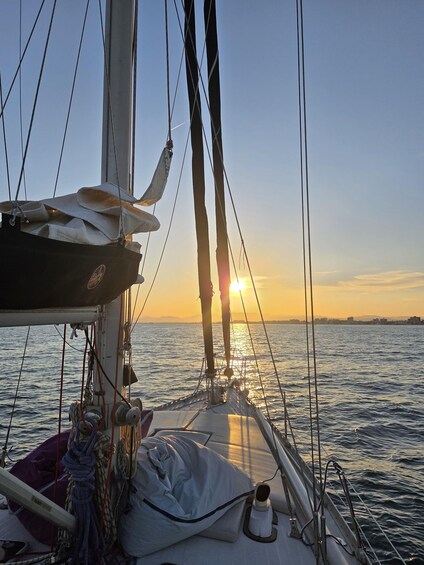 Ein Segelboot bei Sonnenuntergang, die Sonne ist nahe am Horizont, ruhige See und eine entfernte Küstenlinie. 4