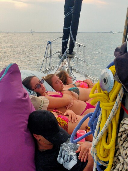 Eine Gruppe von Menschen liegt auf einem Boot und blickt auf das Meer sowie ein entferntes Schiff. 5