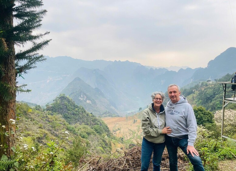 Two people standing on a hill with a mountainous landscape in the background. 3