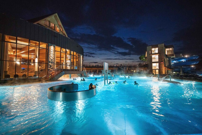Une piscine avec des gens, un bâtiment doté de grandes fenêtres et un bateau à l’arrière-plan. 1
