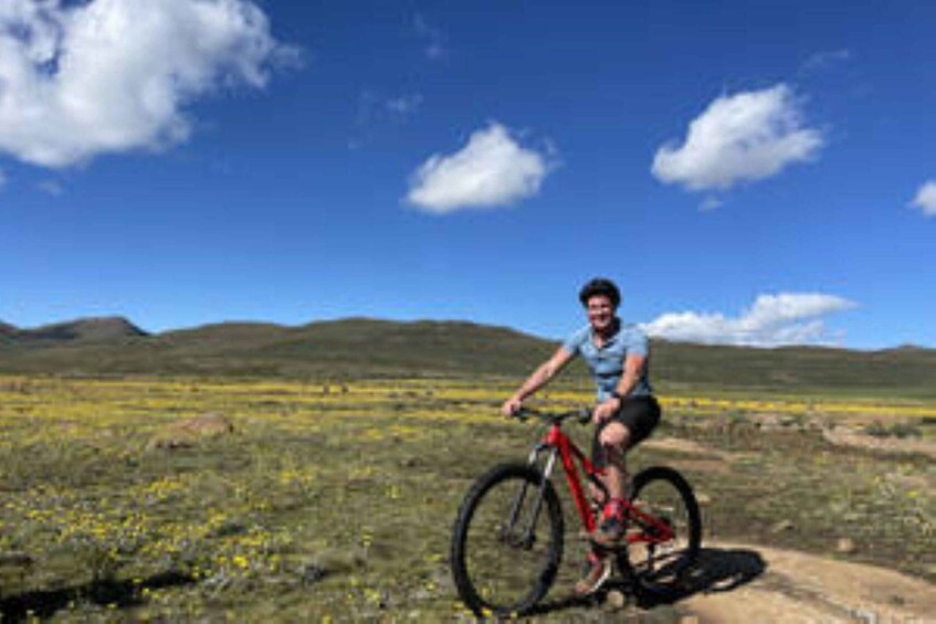 A person riding a red mountain bike on a dirt trail in a grassy field with rolling hills in the background. 5