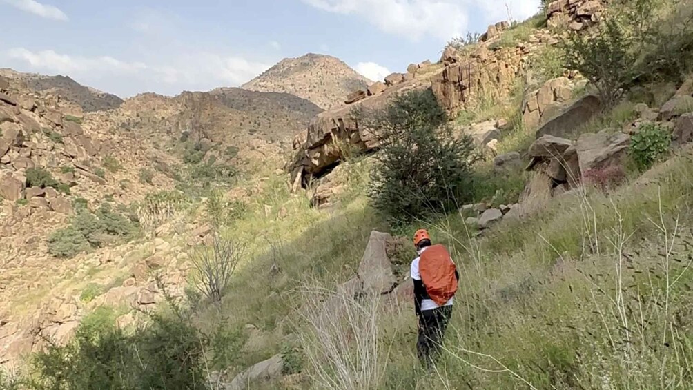 A person hiking in a rocky, hilly terrain with sparse vegetation. 2