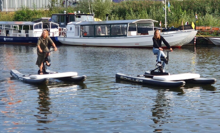 Två personer som åker i uppblåsbara båtar på stilla vatten, med större båtar förtöjda i bakgrunden. 1
