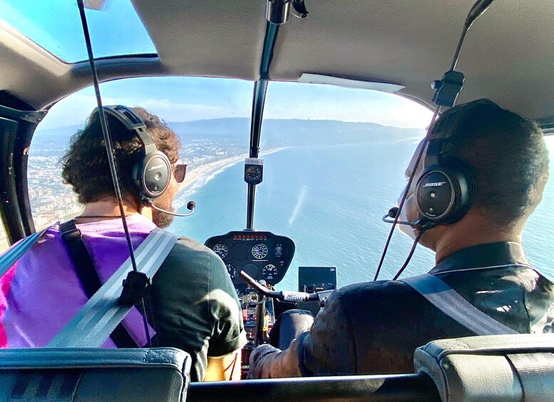 Dos personas en la cabina de un helicóptero con vista a la costa. 1