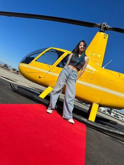 Una persona parada sobre una alfombra roja junto a un helicóptero amarillo con el texto 'Security Helicopters' y 'R44 Lipper II' en su costado. 5