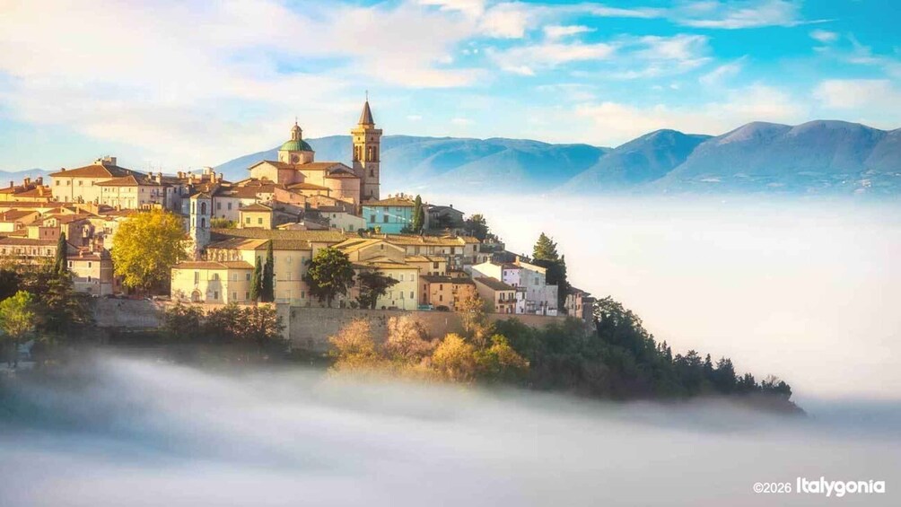 A coastal town with historic buildings, a prominent church, and a tower, surrounded by mountains and fog. 1