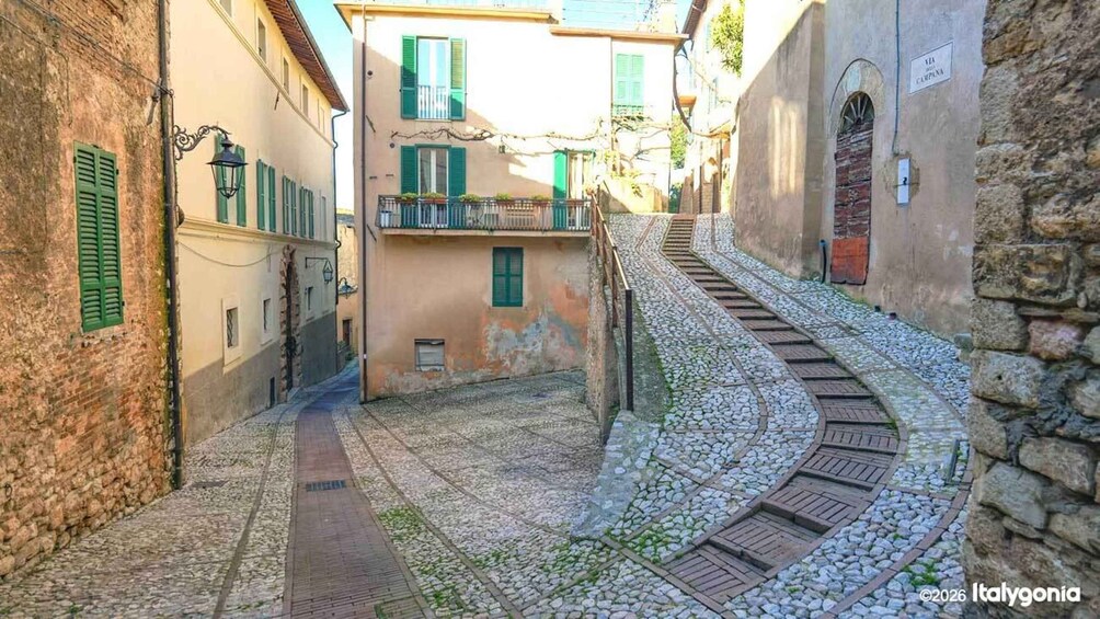 A narrow cobblestone street with buildings on either side, a staircase, and a stone wall. 2