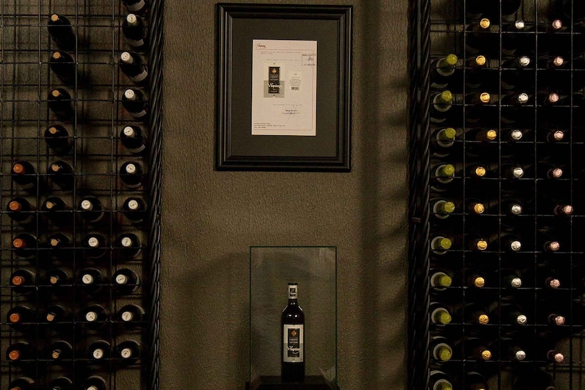 Une cave à vin avec des rangées de bouteilles, un certificat encadré et une bouteille de vin exposée. 1