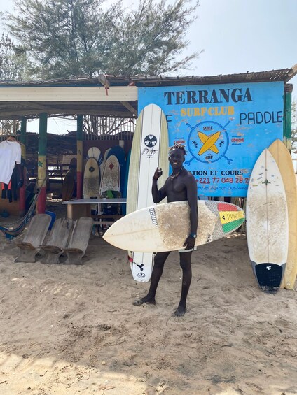 A man holding a surfboard in front of a surf club named 'Terranga Surf Club.' 3