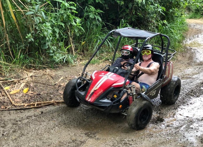 A red off-road vehicle on a muddy path surrounded by greenery. 2