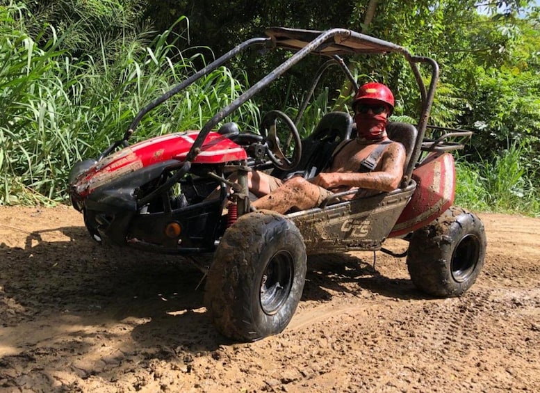 A person in a red and black off-road vehicle on a dirt path surrounded by greenery. 4