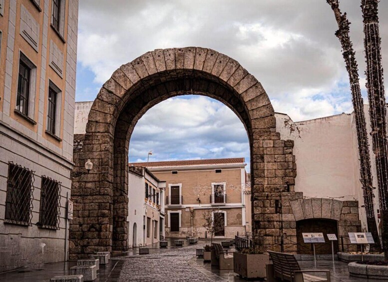 Un ancien arc en pierre, situé dans une place historique d’une ville, bordée de rues pavées et entourée de bâtiments traditionnels. 4