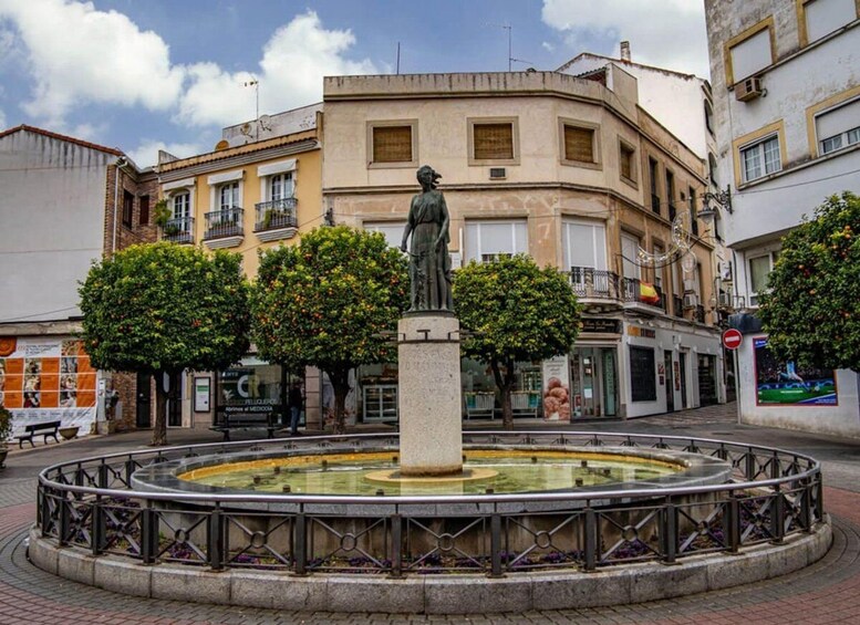 Une statue se trouve au centre d’une fontaine circulaire, entourée d’immeubles et d’arbres. 5