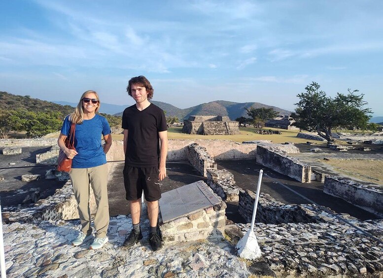 Two people standing on ancient ruins with stone walls and a tree in the background. 1