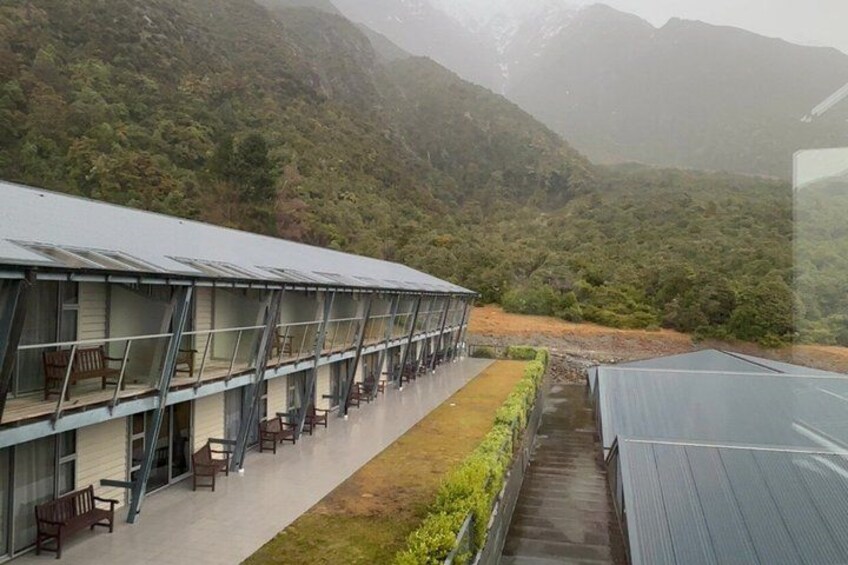 A building with multiple balconies and a covered walkway, surrounded by lush greenery and mountains. 5