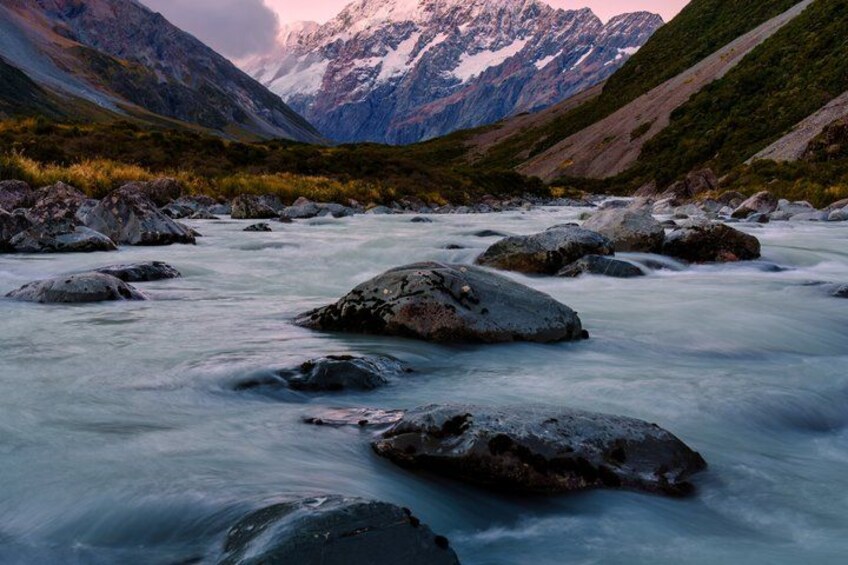 A river with rocks, mountains, and a cloudy sky. 1