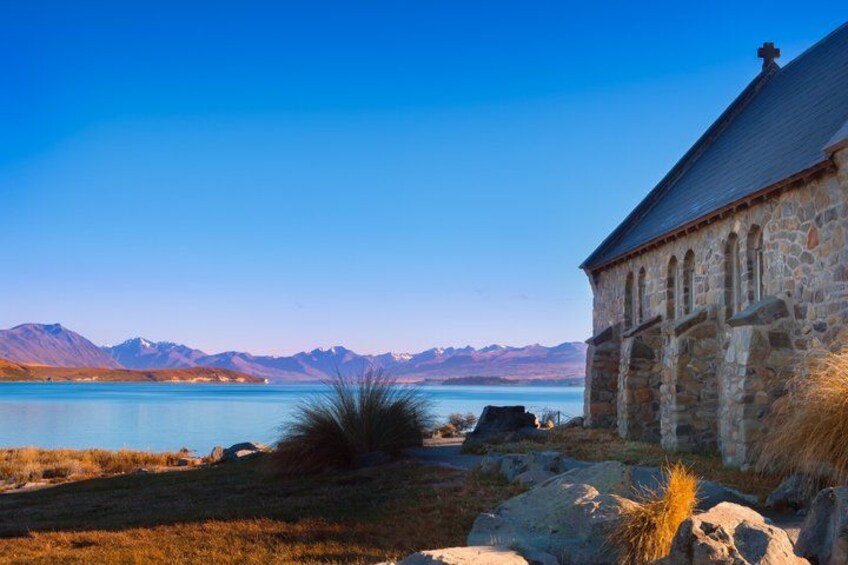 A stone church by a lake with mountains in the background. 2