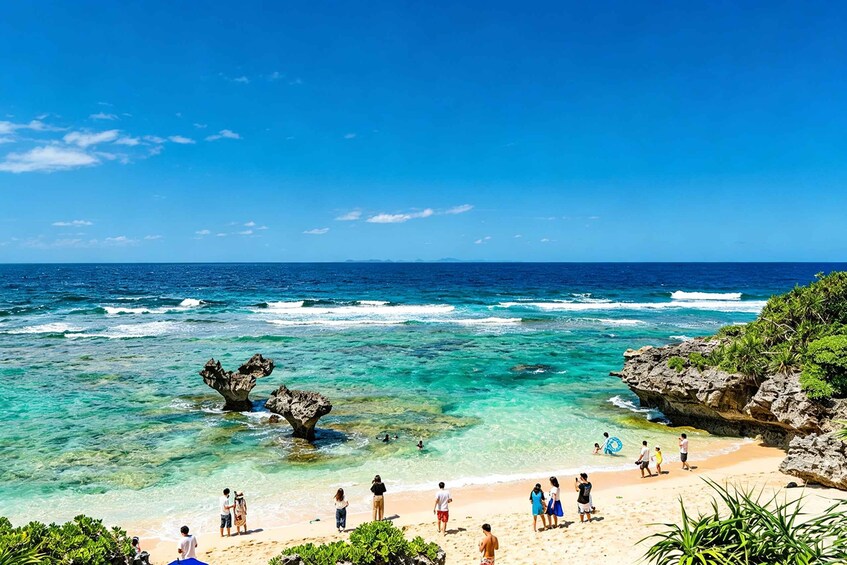 A beach with clear turquoise waters, rocky formations, and people enjoying the sunny weather. 3