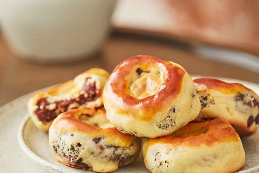 A plate of freshly baked rolls with a golden-brown crust, some with visible seeds and others with a darker filling. 2