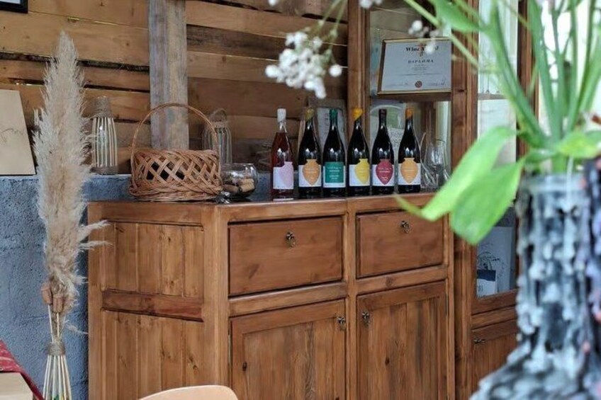 A wooden wine rack with bottles, a basket, pampas grass, and a framed certificate. 5