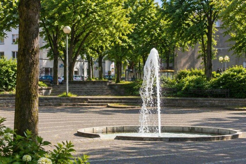A fountain in a park with trees and a building in the background. 3