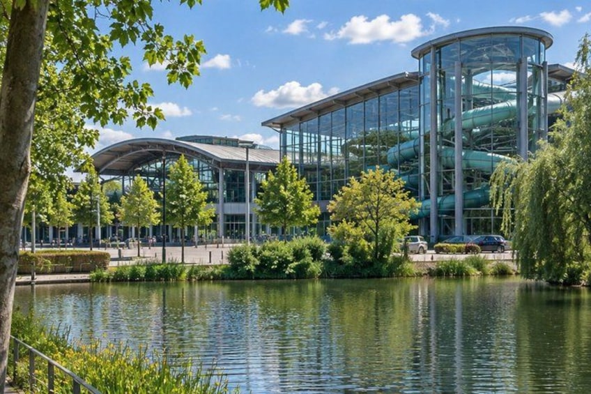 A modern building with a glass facade, a curved roof, and a water feature in front. 5