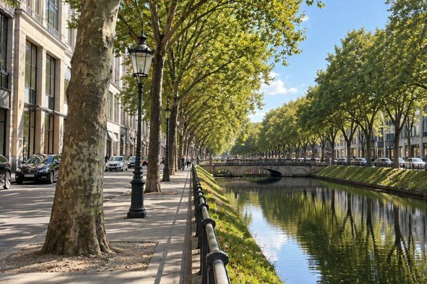 A tree-lined canal with a bridge, buildings, and parked cars. 5