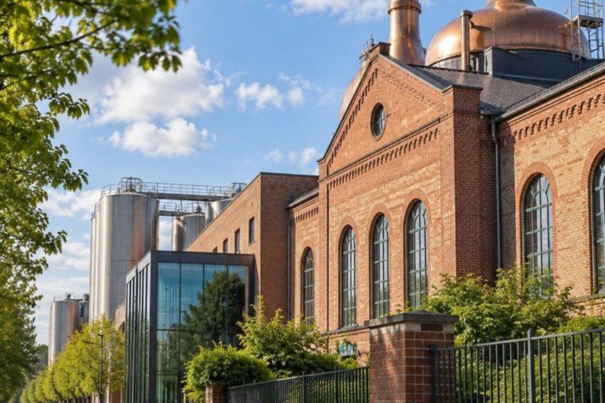 A brick building with large windows and a glass structure, surrounded by trees and metal fences. 3
