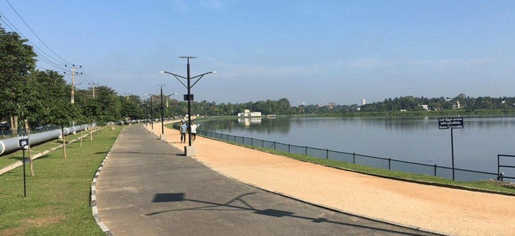 A riverside walkway with a concrete path, metal barriers, and a calm water body. 1