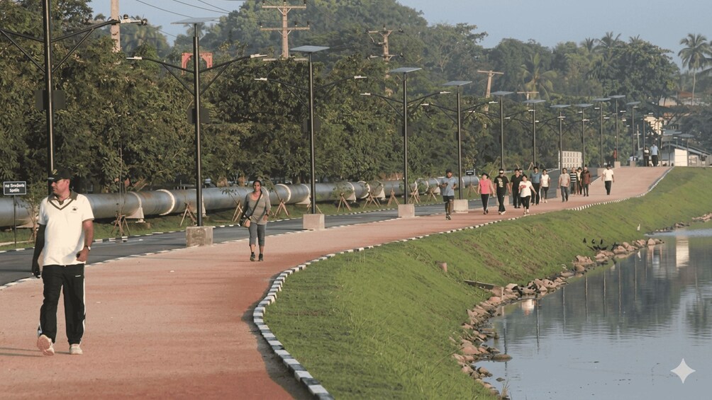 A paved walkway alongside a canal with people walking, street lamps, and industrial structures in the background. 4
