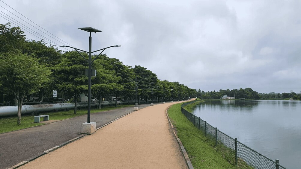 A paved walkway beside a calm river, lined with trees and street lamps. 5