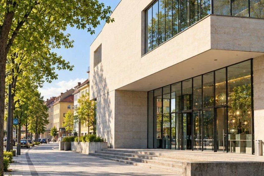 A modern building with large windows, a paved sidewalk, and trees lining the street. 4