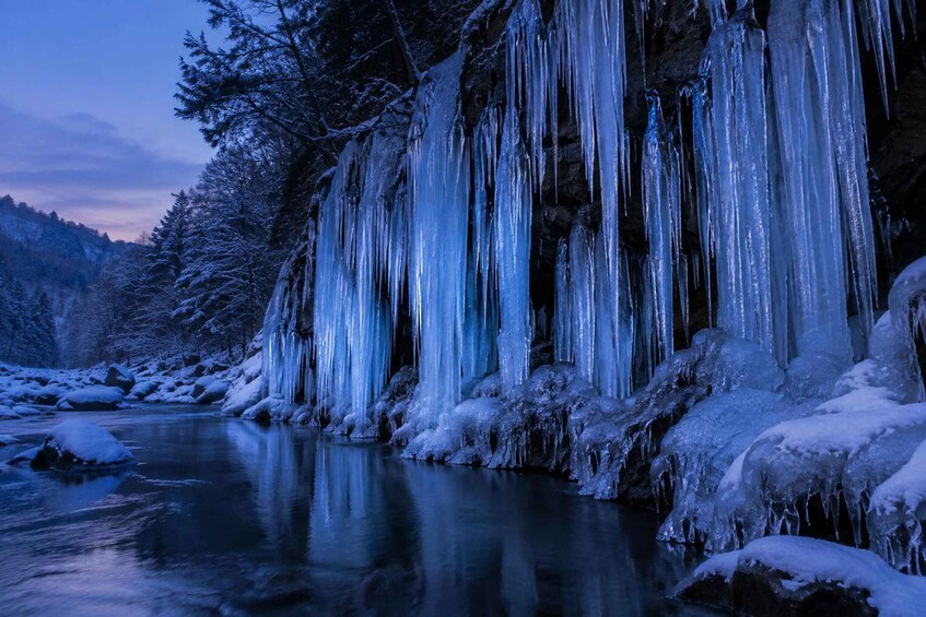 A frozen waterfall with icicles hanging over a river, surrounded by snow-covered trees. 4