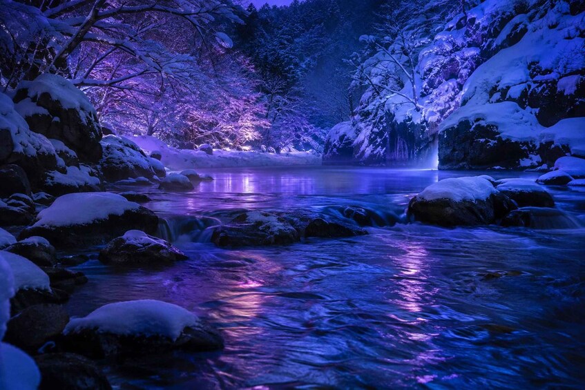 A snow-covered landscape with a flowing river and illuminated trees. 5