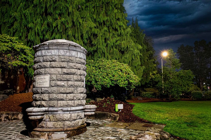 A stone structure with a plaque, surrounded by trees and a well-lit street. 3
