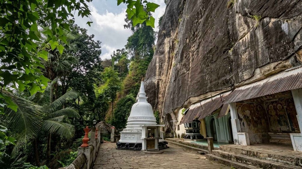 Eine weiße Stupa, umgeben von üppigem Grün und einer felsigen Klippe. 4