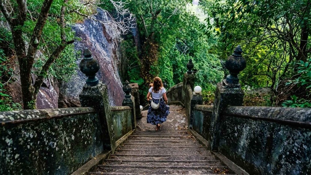 Eine Frau geht eine steile Steintreppe hinunter, umgeben von üppiger Vegetation. 2