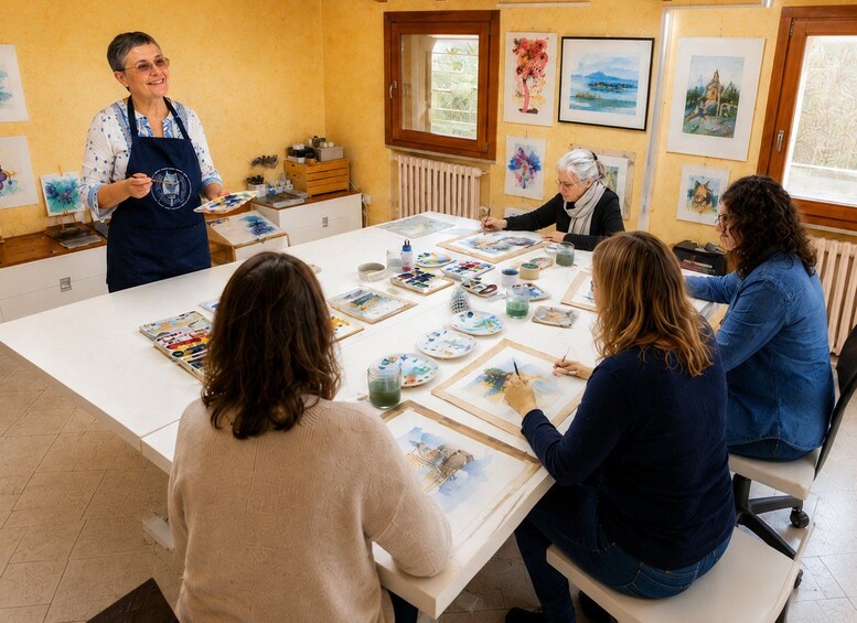 An art class with participants painting on easels, surrounded by art supplies and framed artworks on the walls. 2