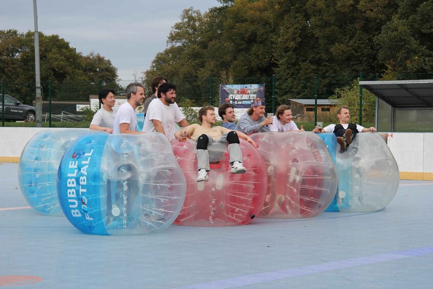 Personas sentadas dentro de tubos inflables transparentes sobre un campo deportivo. 3