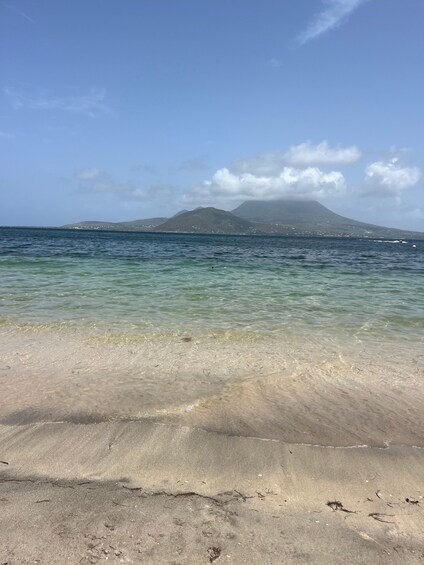 Ein Strand mit klarem Wasser, sandigem Ufer und einem Berg im Hintergrund. 4