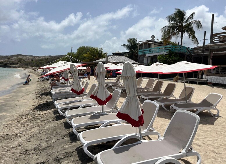 Ein Strand mit Liegestühlen, Sonnenschirmen, Palmen und einem Gebäude im Hintergrund. 1