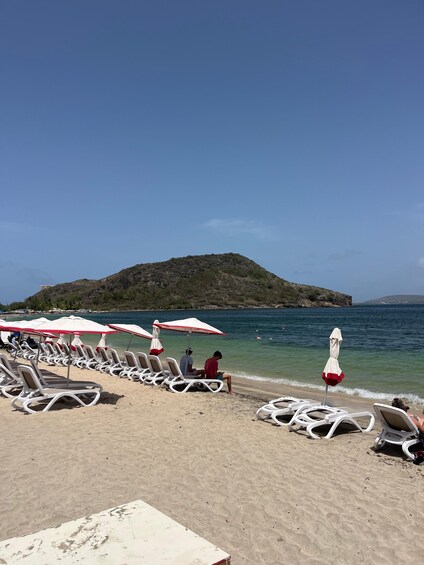 Ein Strand mit Liegestühlen und Sonnenschirmen, ruhigem Meer und einer entfernten Insel. 5