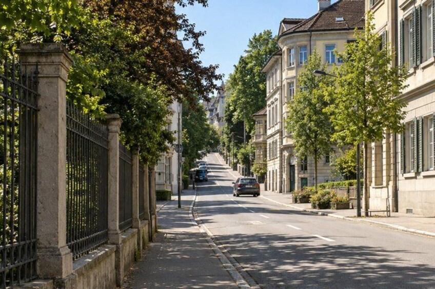 A tree-lined street with parked cars and buildings. 2